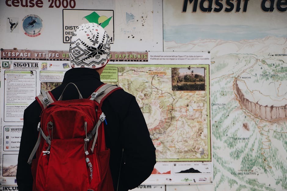 Person with a red backpack studying a detailed trail map in an outdoor mountain setting.