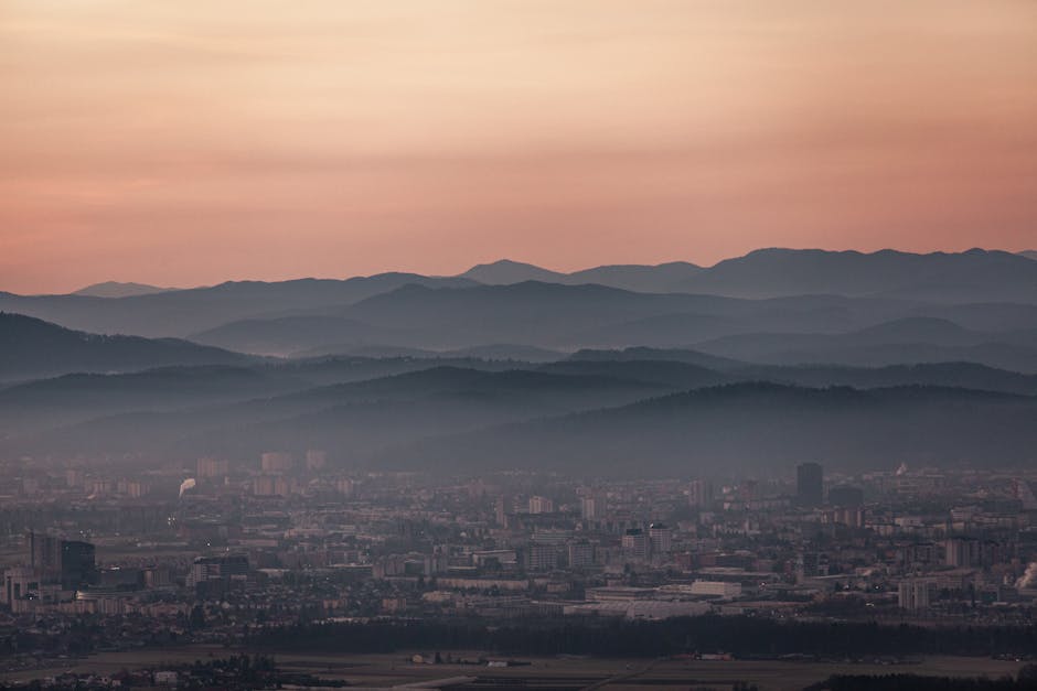 A breathtaking view of a cityscape with overlapping mountain ranges at dusk, showcasing a tranquil urban setting.